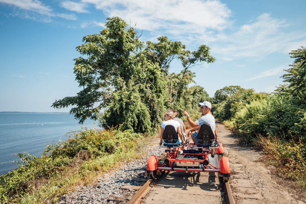 Visitors riding a rail explorer beside the water near Newport
